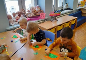 Grupa dzieci przy stoliku wykonuje dinozaura